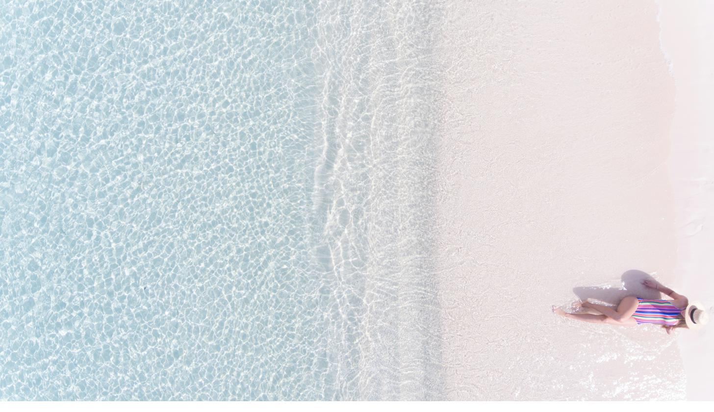 A woman resting at the edge of shallow, clear water on a white sand beach